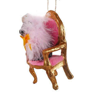 A fluffy white and pink feathered dog ornament seated in a gold farmstead bull ornament chair with pink cushioning