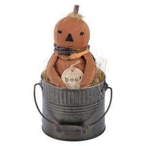 Brown fabric boo doll pumpkin with black embroidered face and plaid scarf nestled in hay in a metal bucket halloween dolls