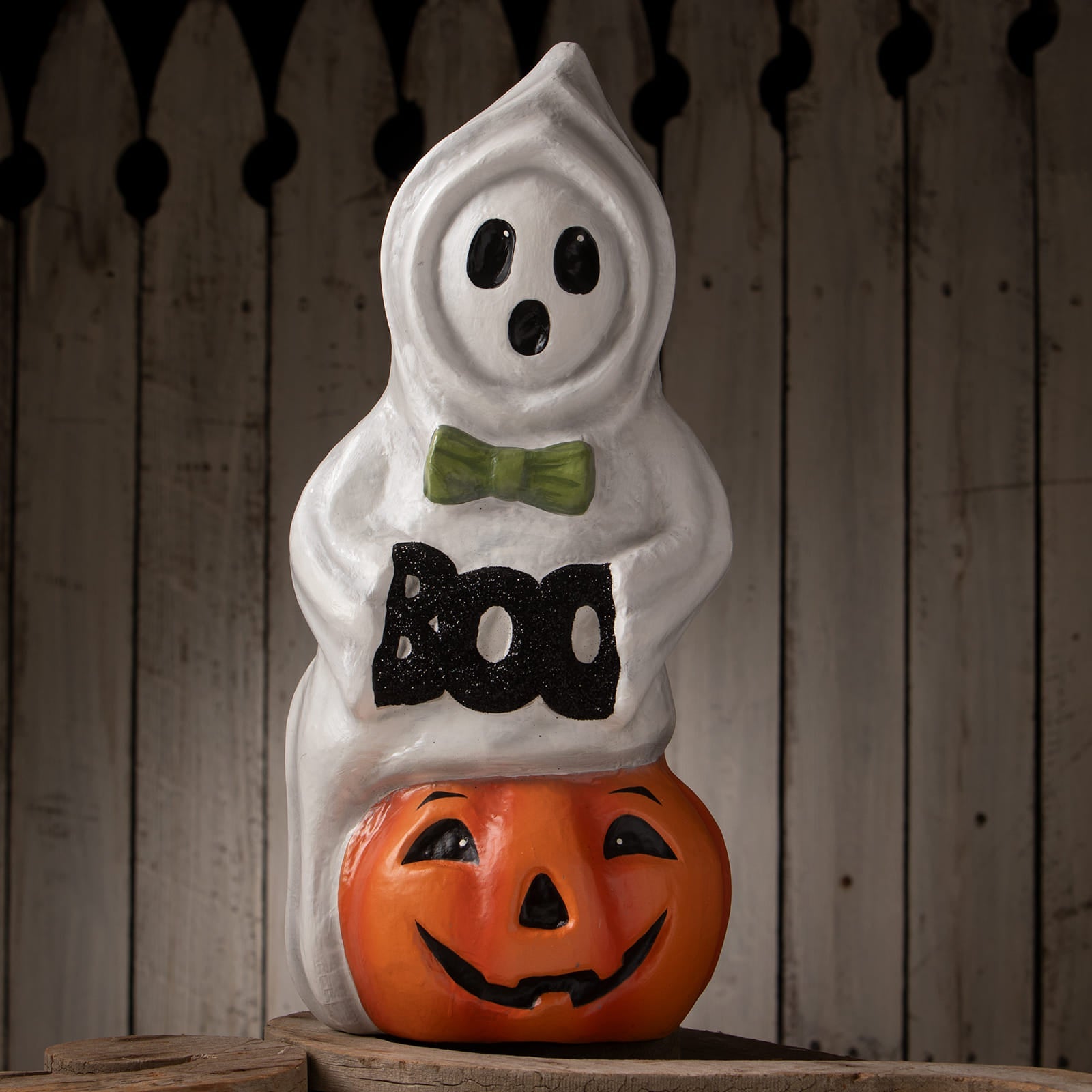 White ghost figurine with black eyes and mouth wearing green bow tie and boo text on jack o lantern halloween ghost figures decor
