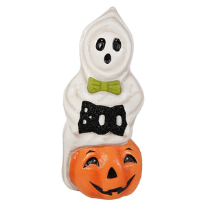 White ceramic halloween ghost figure with green bowtie holding black glittery boo sign on orange jack o lantern pumpkin