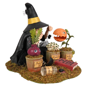 Black botany witch figurine with yellow-striped hat and cloak tending whimsical potted plants perfect for halloween witches decor