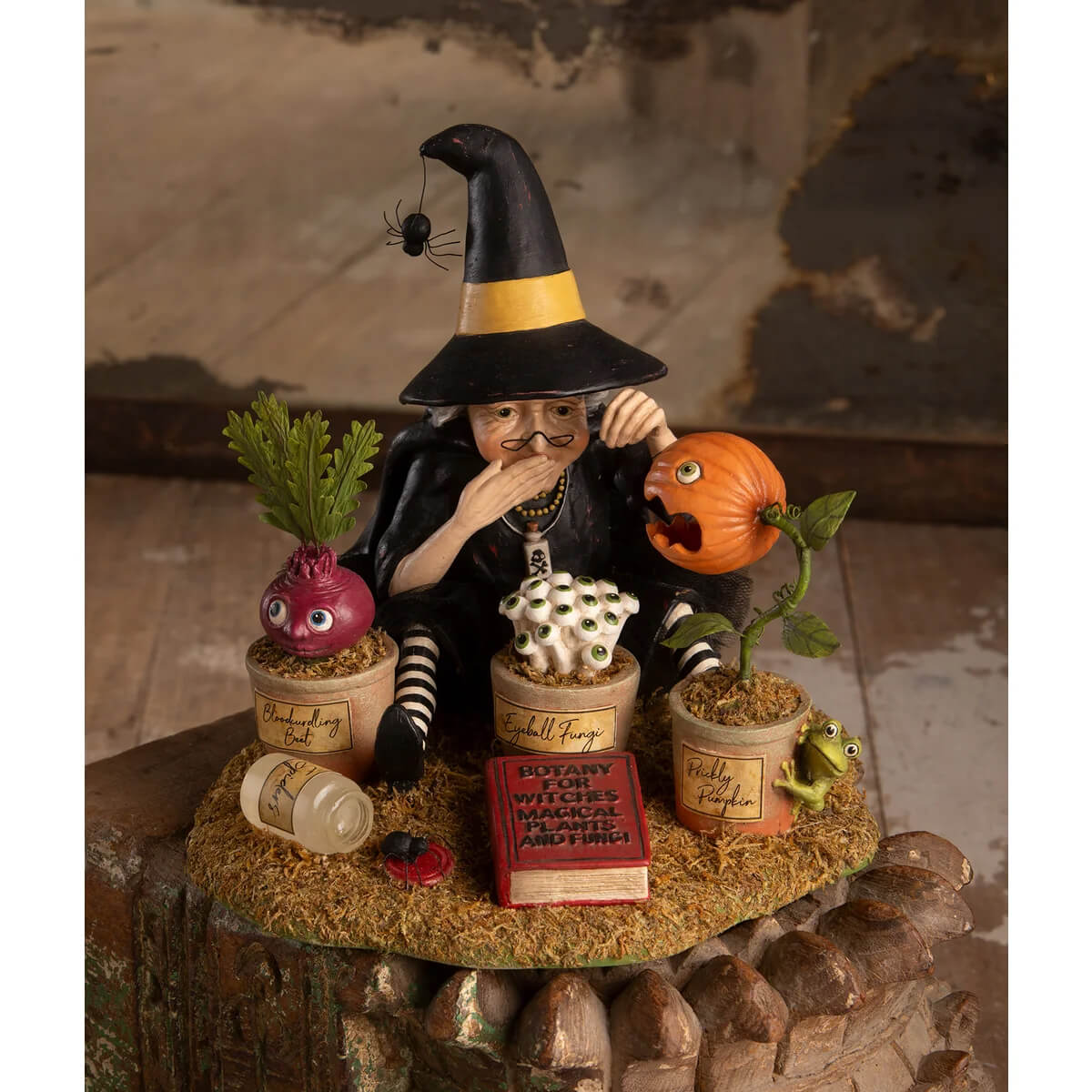 Botany witch figurine with yellow-striped hat and stockings seated among whimsical potted plants for halloween witches