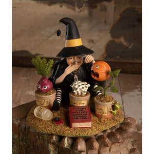 Botany witch figurine with yellow-striped hat and stockings seated among whimsical potted plants for halloween witches