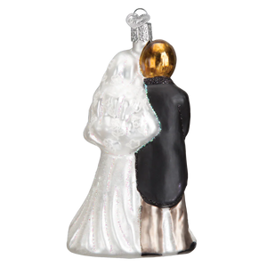 A glass bridal couple ornament featuring a bride in white gown and groom in black suit with gold heads perfect as tree toppers or lighted decor