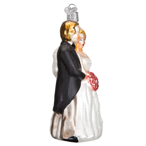 Glass bridal couple ornament featuring a bride in white gown holding red bouquet and groom in black tuxedo for tree toppers