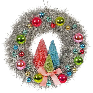 A festive brights tinsel wreath with silver tinsel colorful glass ornaments and miniature painted pine trees tied with pink ribbon
