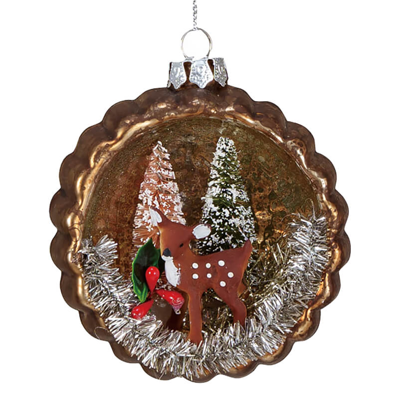 Christmas tree ornament featuring a winter scene with a reindeer and trees inside a round, scalloped frame.