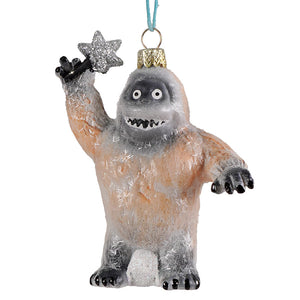 A glittery translucent glass ornament with a friendly peach and gray abominable snow monster holding a silver star by cody foster