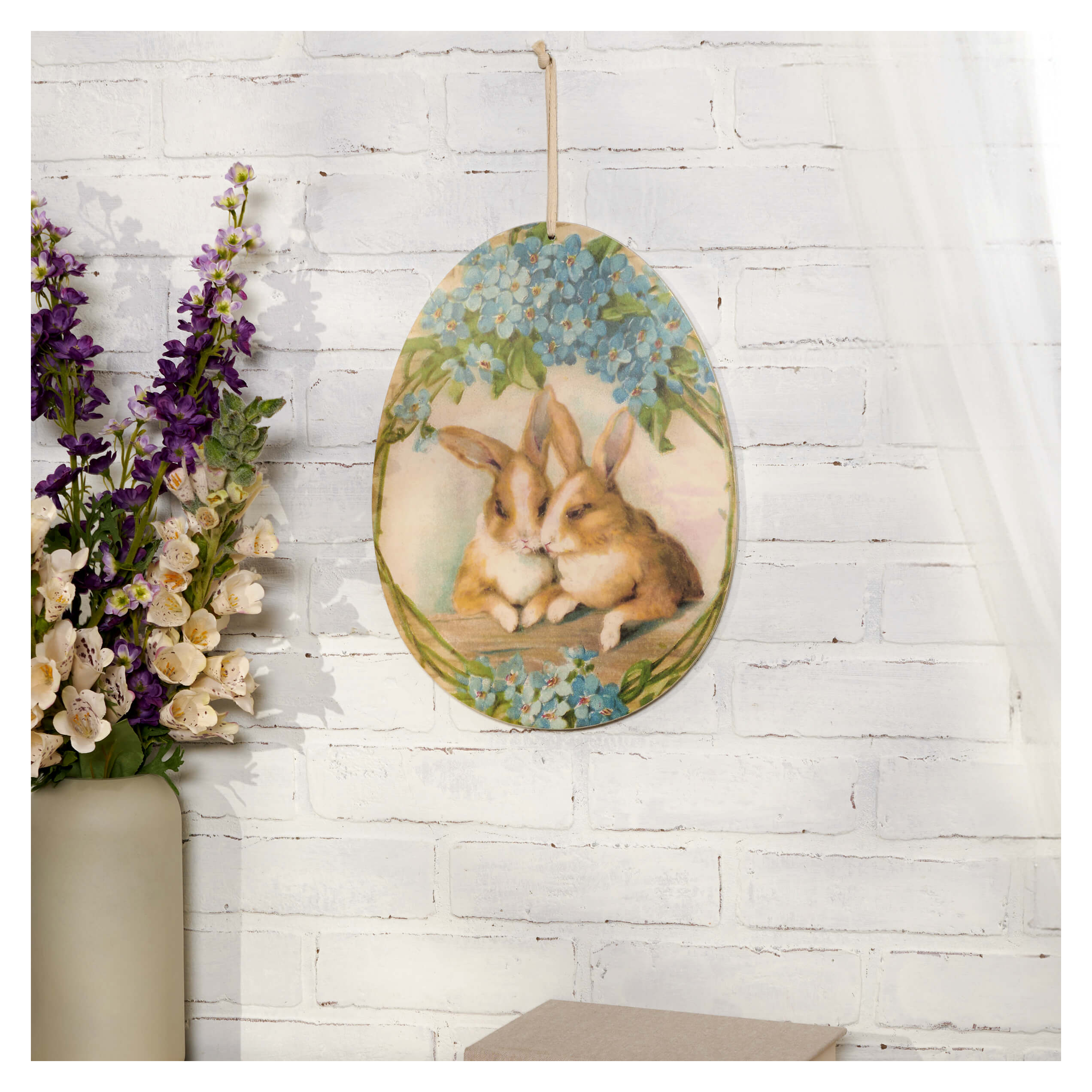 Elegant egg shaped hanging wooden wall decor with two brown rabbits nestled under blue spring flowers hydrangeas