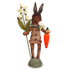 Brown bunny face garden hare figure in a buttoned coat holding white tulips and an orange carrot folk art style