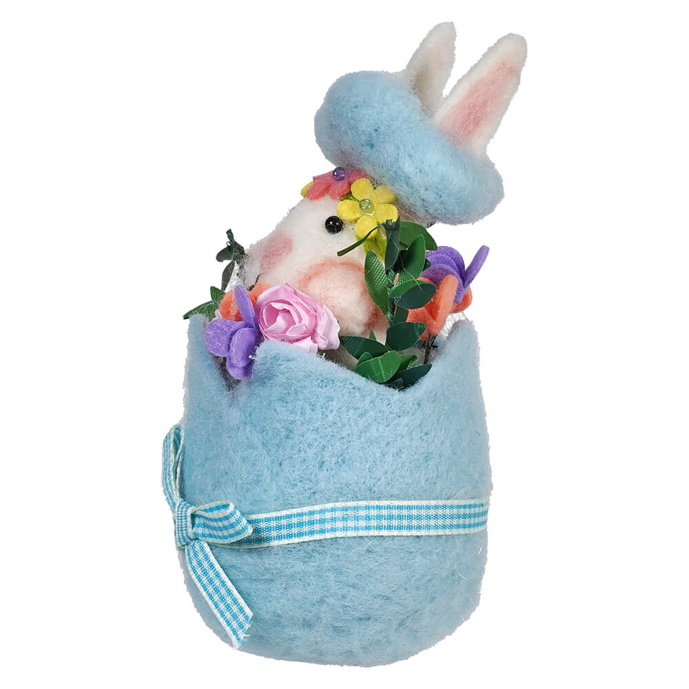 Decorative Easter bunny emerging from a light blue egg with a gingham ribbon and floral accents.