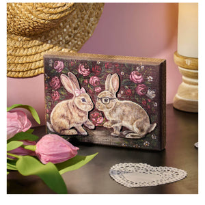 Rustic wooden bunny love block sign with two illustrated rabbits and painted roses on dark textured wood background