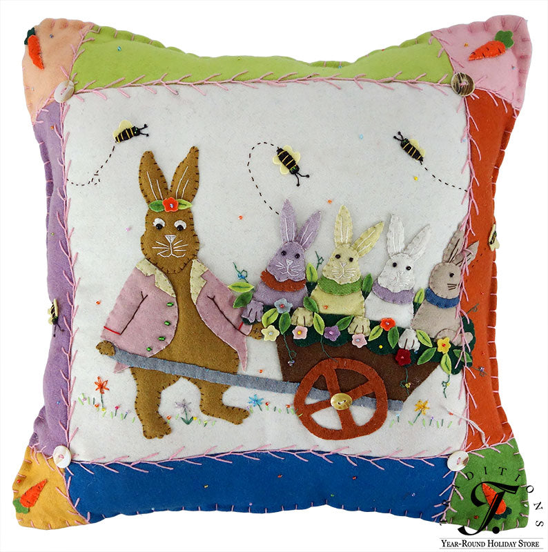 A felt wheelbarrow pillow with a brown rabbit in a pink coat and colorful bunnies perfect for easter pillows