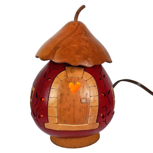 A hand-crafted lighted gourd shaped like a red and brown fairy house with a heart window by meadowbrooke gourds artisans