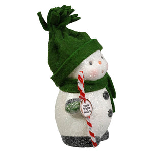 A glittery white bethany lowe designs snowboy figurine with a green felt hat and scarf holding a candy cane