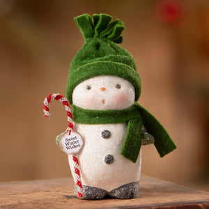 A charming white snowboy figurine by bethany lowe designs with a green velvet hat scarf holding a candy cane