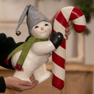 A festive white glittery christmas snowman figure wearing a silver jester hat and green scarf holding a candy cane