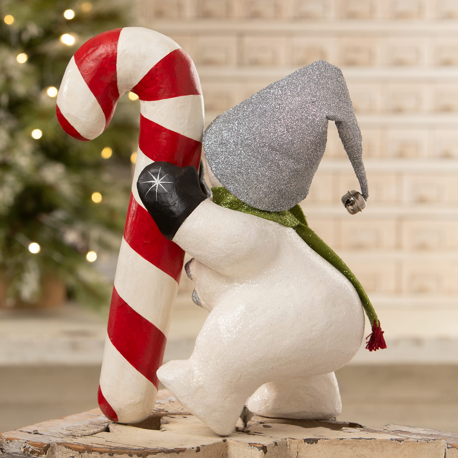 A festive white christmas snowman figure with a glittery silver hat and green scarf holding a candy cane decor