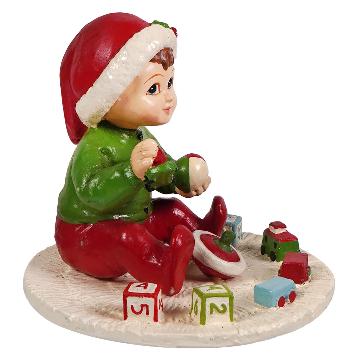 A glossy resin baby elf figurine in a red santa hat and green outfit sitting on snow with colorful blocks by bethany lowe designs