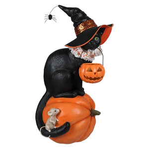 Black witch cat figurine with green eyes wearing a glittery hat holding an orange jack-o-lantern for halloween witches decor