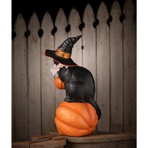 Black cat witch figurine with glittery orange hat band sitting on a bright orange pumpkin halloween witch decor