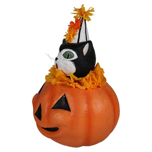 A black and white cat with green eyes wearing a striped party hat sits on an orange pumpkin in cecil’s hang out pm
