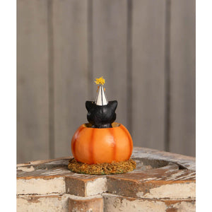 A black cat figurine wearing a white and silver party hat with yellow tassels sits in an orange pumpkin container in cecil’s hang out