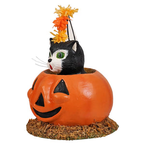 A black and white cat with green eyes peeks out from a bright orange pumpkin planter with a party hat in Cecil’s Hang Out