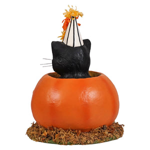A black cat figurine wearing a white and orange striped party hat sits in an orange pumpkin planter with mossy base cecil’s hang out