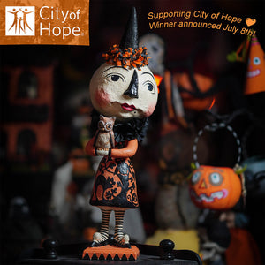 A whimsical johanna parker witch figurine in orange and black holding an owl for charity raffle summerween candy corn spooks