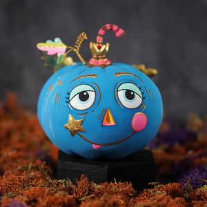 A cheery blue pixie pumpkin painted blue with expressive eyes star-shaped cheek and gold decorative accents