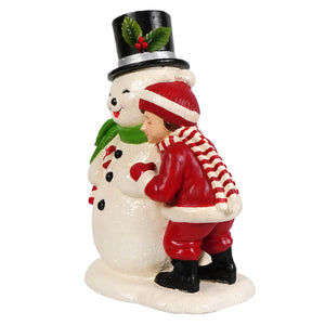 A cheerful white bethany lowe designs child hugging snowman with black top hat and green scarf in festive decor