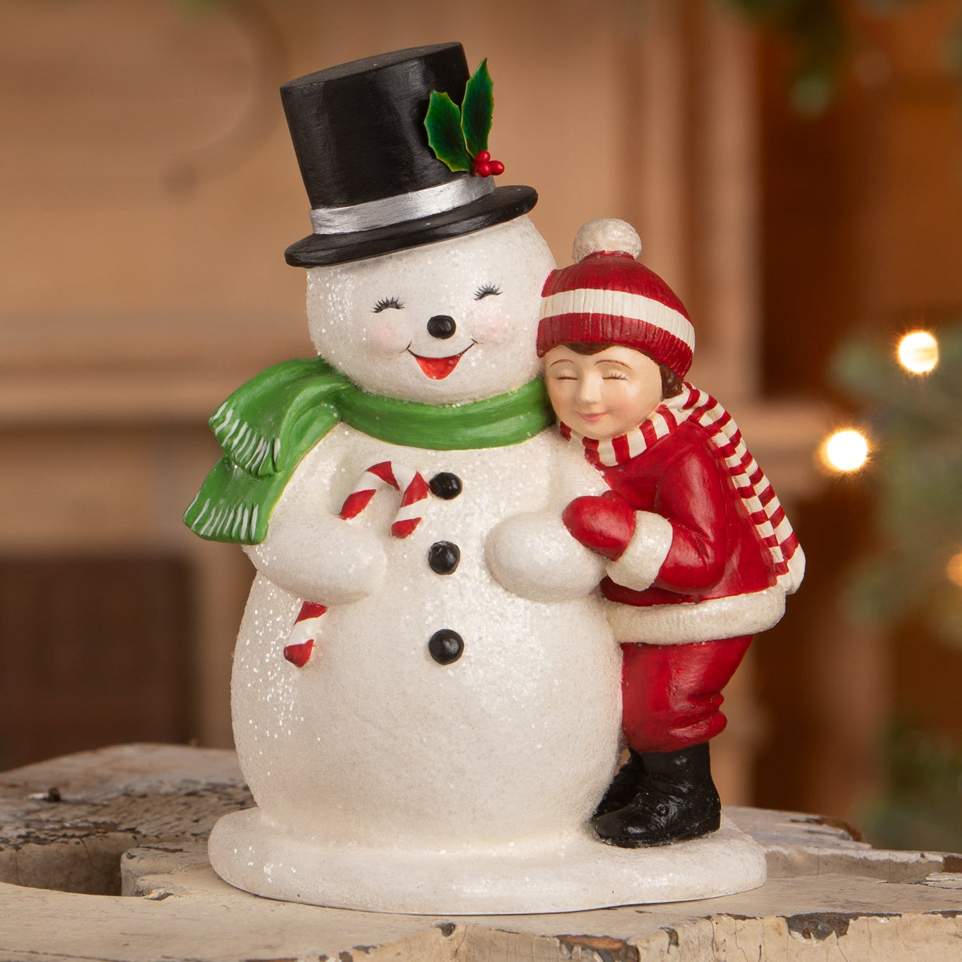 A cheerful child hugging a white bethany lowe designs snowman figurine with holly hat and candy cane details in winter attire