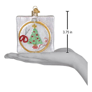 A clear glass christmas cross stitch ornament with a green tree red stars and gold hoop figural decor ideal for tree toppers