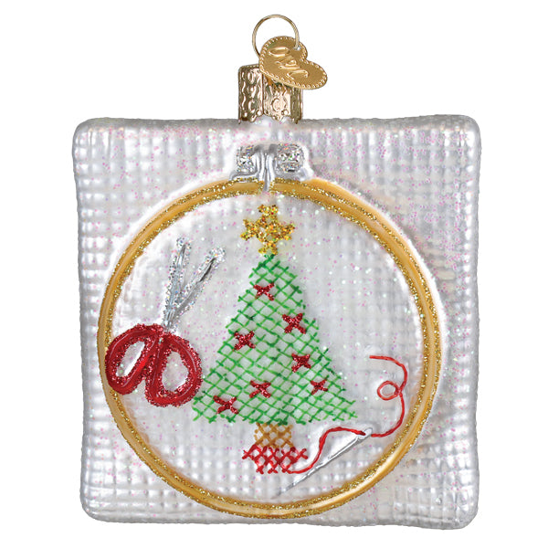 A clear glass christmas cross stitch ornament with a gold hoop and stitched tree perfect for figural decor or tree toppers