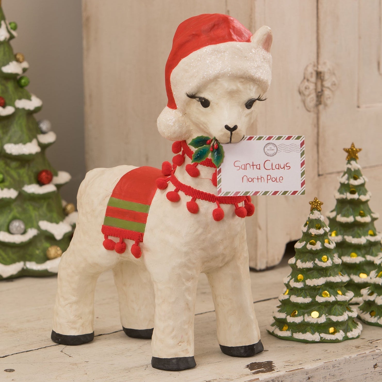 Christmas llama figural decor by bethany lowe is a white alpaca with red santa hat and scarf holding a north pole card