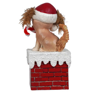 A dog wearing a Santa hat sits atop a brick chimney with snow-covered edges.