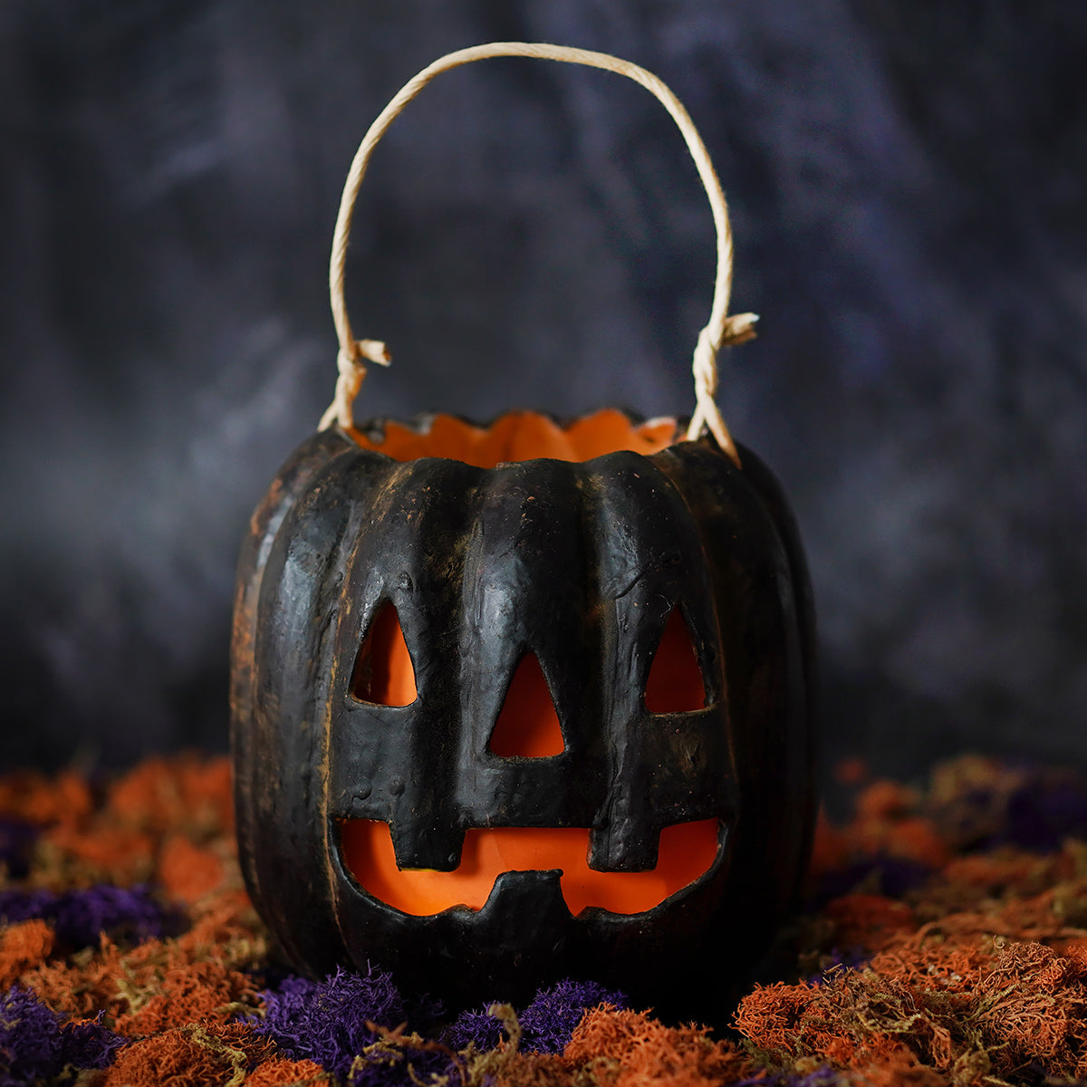 Classic jack face black pumpkin bucket with woven handle and glowing orange interior from muffin junction