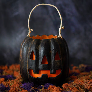 Classic jack face black pumpkin bucket with woven handle and glowing orange interior from muffin junction