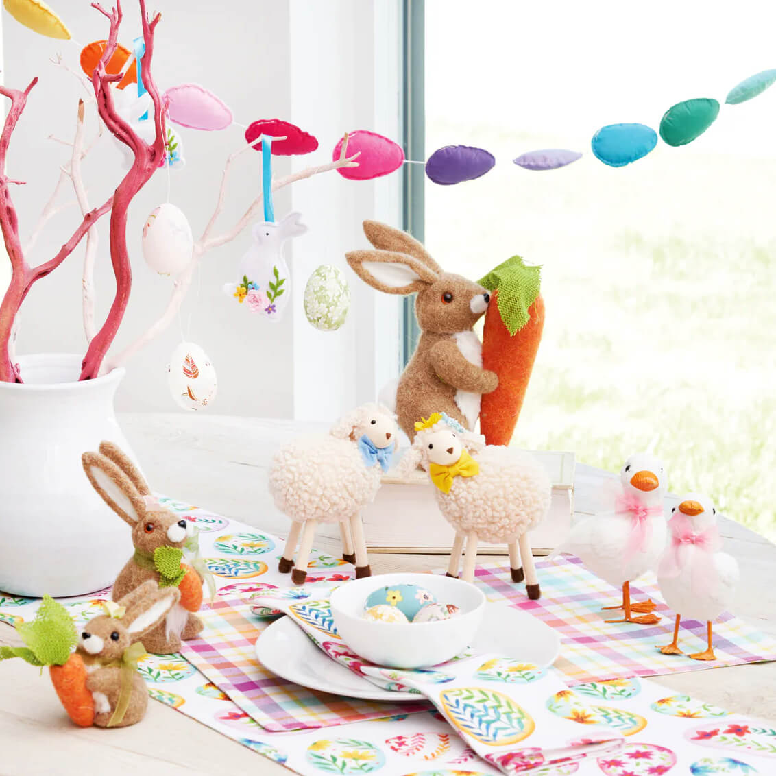 Easter-themed table setting with decorative bunnies, lambs, and colorful egg garland.