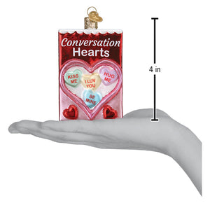 A red and pink glass conversation heart ornament shaped like a candy box with colorful heart messages inside