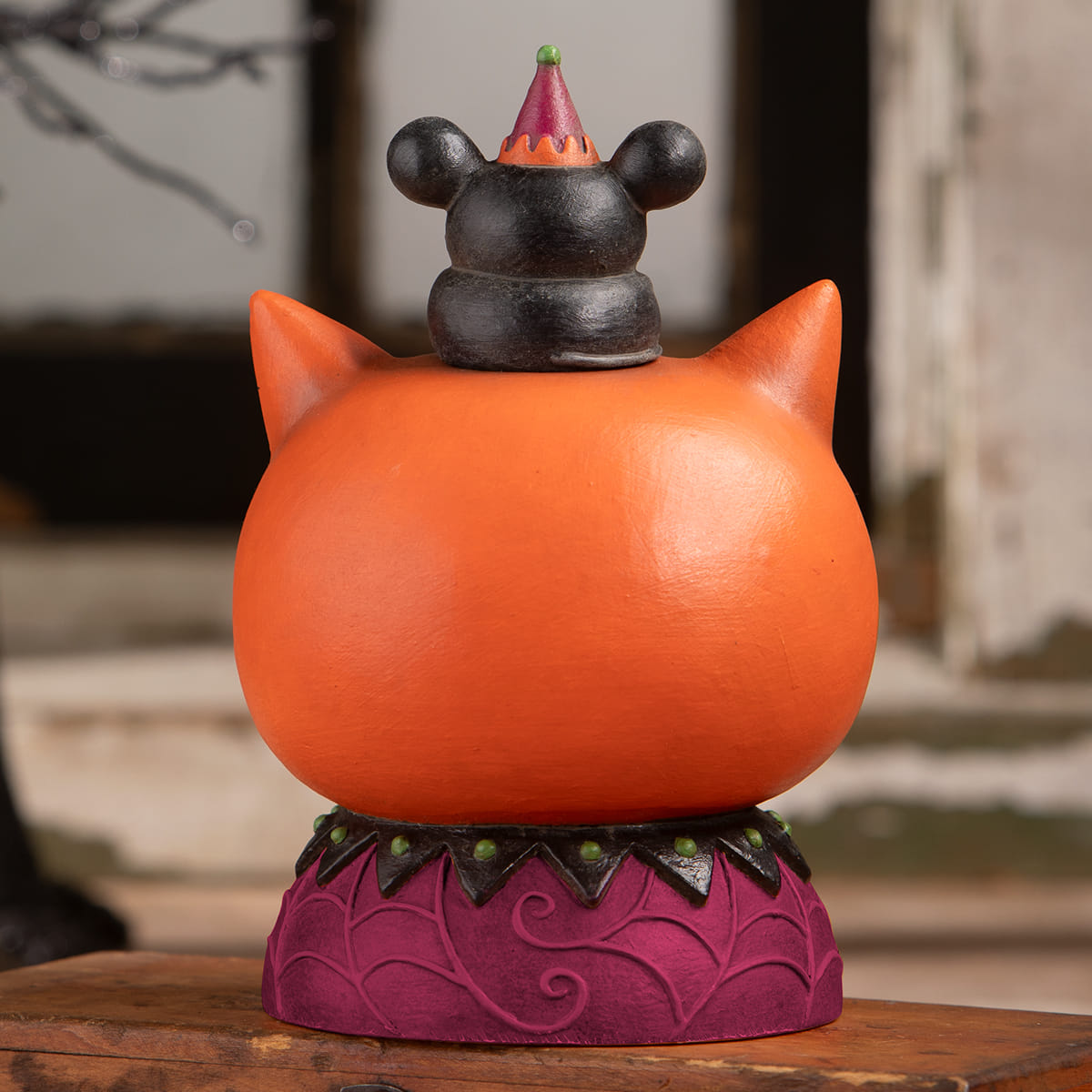 Orange copper cat figurine with black ears and halloween cats mickey mouse head wearing red party hat on purple base