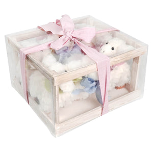A clear plastic gift box with a light wood frame tied with a pink ribbon holding a sheep boxed set for spreading holiday cheer