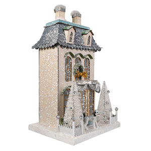 A festive cream and white chateau house ornament with snow dusting and frosted trees for a christmas village display