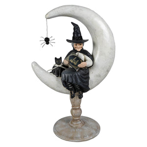 A whimsical moon moira witch figurine in black cloak on a weathered white crescent moon holding a gold detailed book
