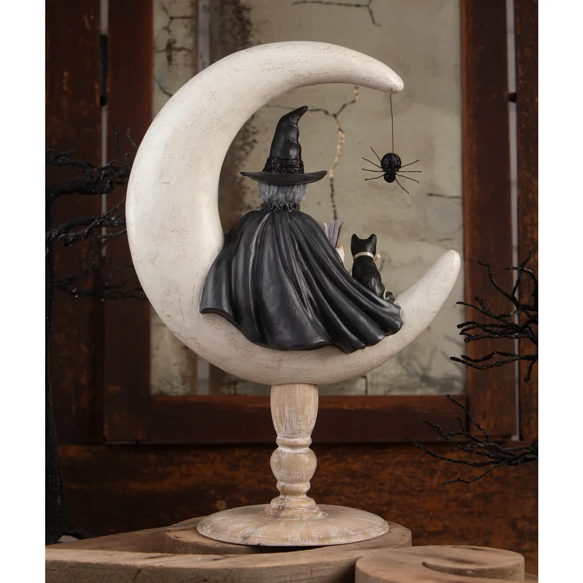 A crescent moon moira witch sits in a black hat and cape with a black cat and spider halloween witches decor