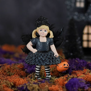 Black crow hazel girl witch figurine with blonde pigtails, glittery dress, striped stockings, holding orange pumpkin bucket