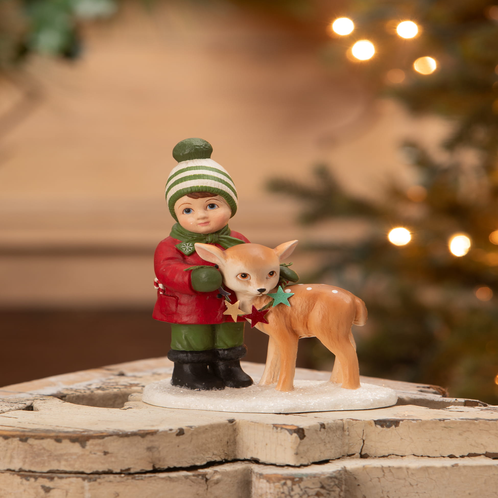 A charming bethany lowe designs miniature figurine of a child in a red coat holding a deer with star ornaments