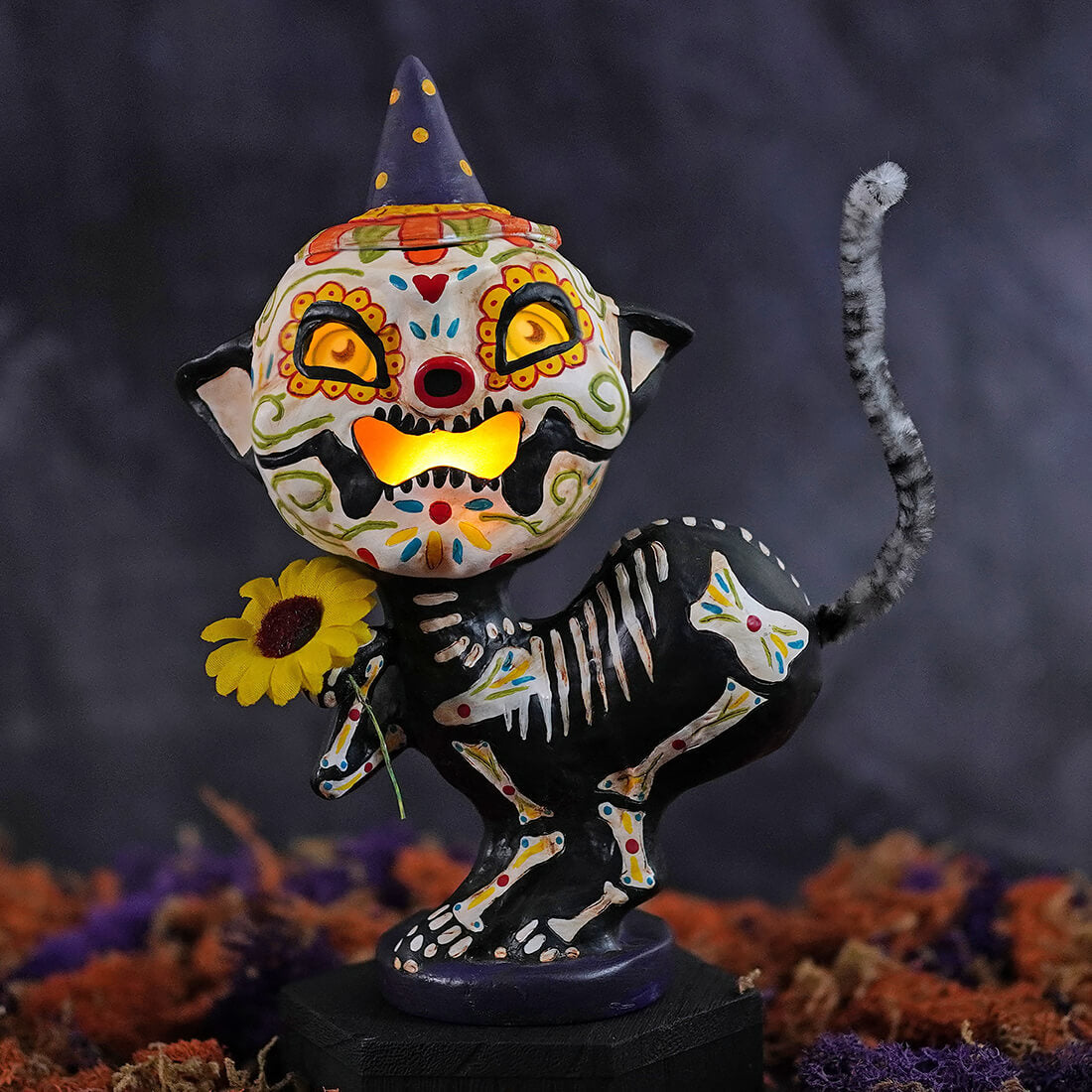 A whimsical black cat day of the dead kitty luminary with sugar skull face purple hat and sunflower halloween luminaries