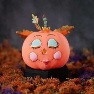 A whimsical demure peachy pink pixie pumpkin figurine with turquoise eyes pink cheeks and a feather crown perfect for pumpkin pixie display